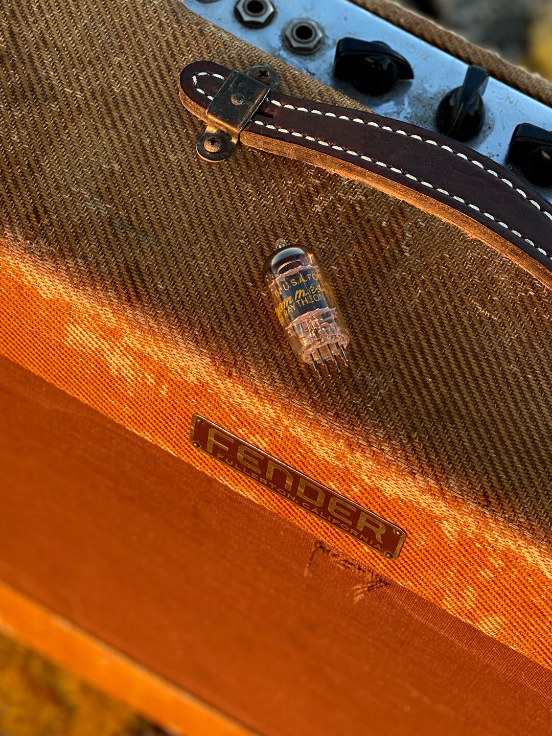A vintage vacuum tube on top of a tweed Fender amp