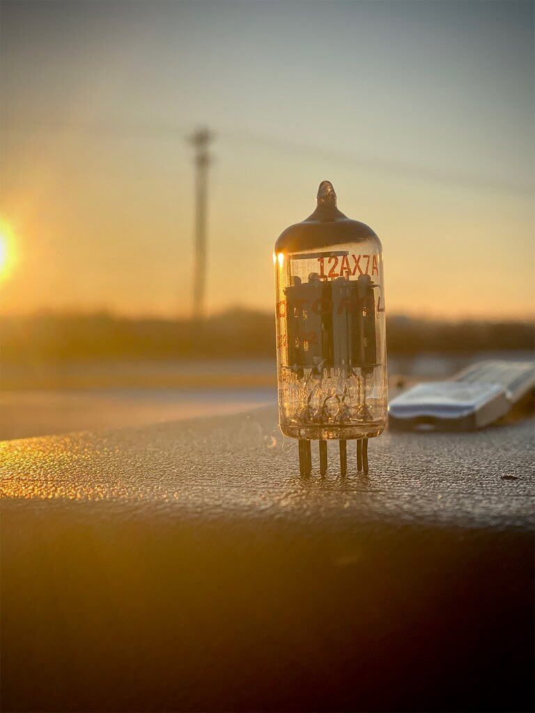 A vintage NOS tube on top of an amp set against a sunset scene